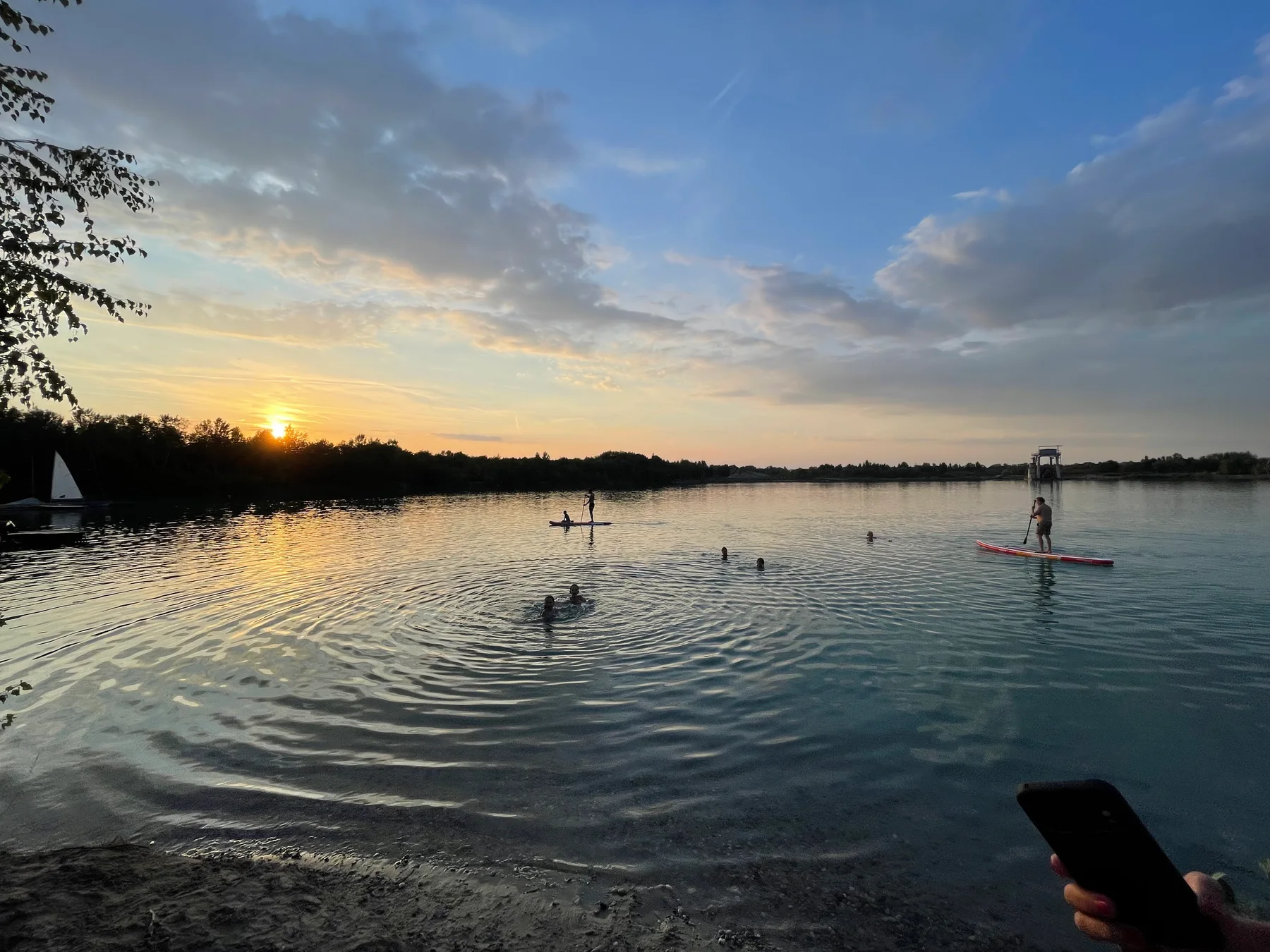 Sonnenuntergang über dem Baggersee mit einem Stand-up-Paddler in der Ferne